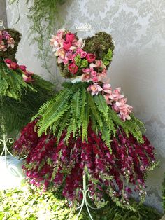 two teddy bears made out of flowers and moss sitting on top of each other in front of a wall