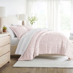 a bed with pink and white comforters in a bedroom next to a window,