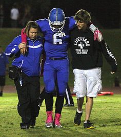 two football players are being carried off the field by an umpire and another player in blue