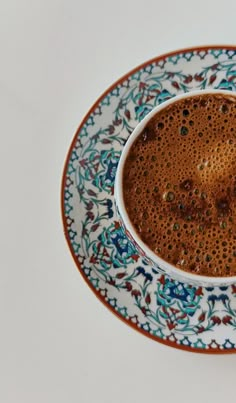 a cup of hot chocolate on top of a blue and white plate with an ornate design