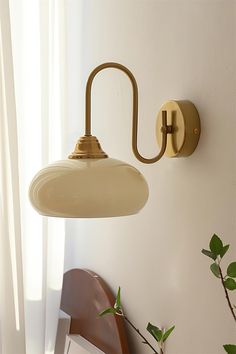 a wall light that is on the side of a wall next to a chair and potted plant