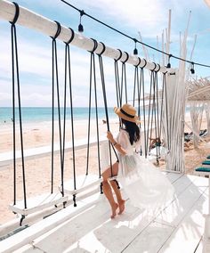 a woman in a straw hat is sitting on a hammock at the beach