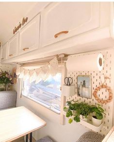 the inside of a camper with plants on the windowsill and small tables in front of it