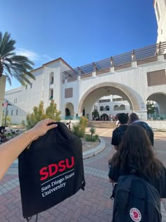 someone holding up a black bag with sdsu on it in front of a building