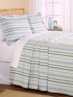 a bed with blue and green striped comforters in a room next to a window