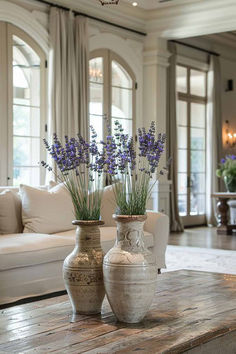 two vases with lavender flowers are sitting on a table in front of a couch