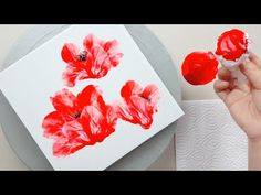 someone is painting red flowers on a white paper and then they are covered with wax