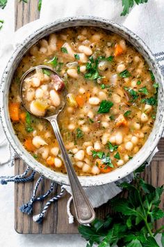 a white bowl filled with beans, carrots and parsley on top of a cutting board