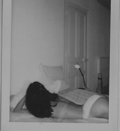 black and white photograph of a woman laying on a bed with her back turned to the camera