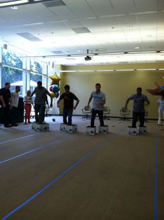 several people are standing on skateboards in an empty room while others stand and watch