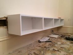 a white shelf sitting on top of a floor next to a drywalling wall