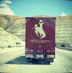 the back end of a semi truck driving on a highway with mountains in the background