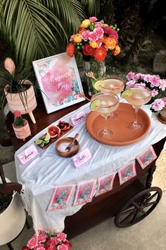 a table topped with two wine glasses next to a sign that says tropical fiesta margarita bar