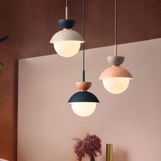 three different colored lights hanging from the ceiling above a table with flowers in vases