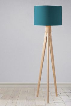 a wooden floor lamp with a teal shade on the top, and a white wall in the background