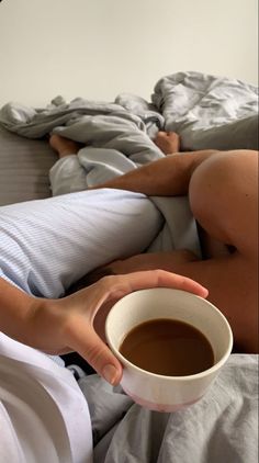 a person laying in bed holding a cup of coffee