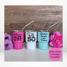 three different colored tumblers with the words cheers on them and two pink flowers in front