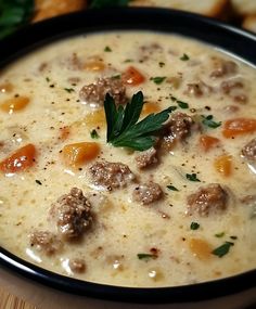 a bowl of soup with meatballs, carrots and parsley in it on a wooden table