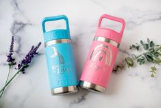 two insulated water bottles sitting next to each other on a marble surface with flowers