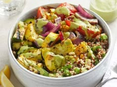 a white bowl filled with vegetables next to lemon wedges and a glass of green juice