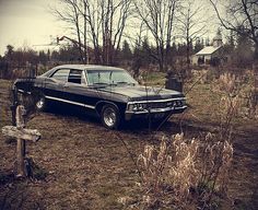 an old car is parked in the middle of a field next to a wooden cross