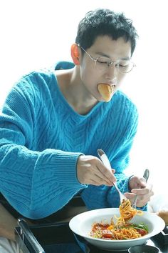 a man sitting at a table eating spaghetti from a bowl with a fork in his mouth