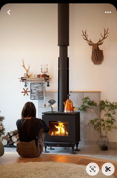 a woman sitting on the floor in front of a fire place with deer heads above it