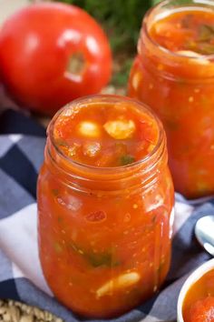 two mason jars filled with tomato soup on top of a blue and white checkered towel