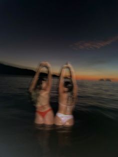 two women in bikinis are standing in the water with their hands above their heads