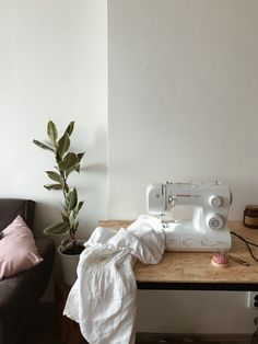 a white sewing machine sitting on top of a wooden table next to a potted plant