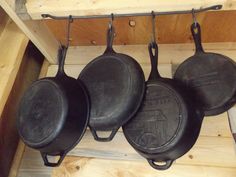 three cast iron skillets hanging from hooks on a wooden shelf next to wood planks