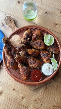 a plate with chicken wings and dipping sauces on it next to a glass of water