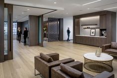 two people are walking in the lobby of an office building with wood floors and furniture