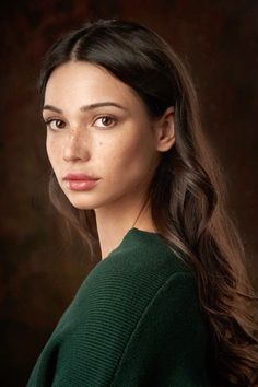 a woman with long hair wearing a green sweater and looking at the camera while standing in front of a dark background