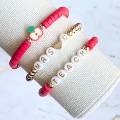 two personalized bracelets with apple charms are on display in front of a pair of white gloves