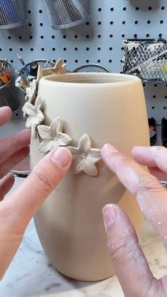 two hands are working on a clay vase