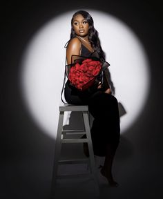 a woman sitting on top of a stool holding a bouquet of roses