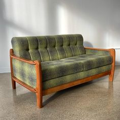 a green couch sitting on top of a floor next to a white wall in an empty room