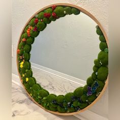 a circular mirror with green moss and butterflies on it, sitting on a counter top