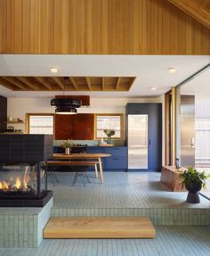 an open kitchen and living room with blue tile flooring, wood paneled walls and fireplace