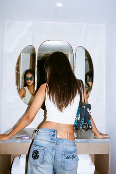 a woman standing in front of a mirror looking at herself in the mirror with her back to the camera