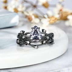 a white diamond ring sitting on top of a marble slab with flowers in the background