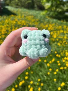 a hand holding up a small stuffed animal in the middle of a field of yellow flowers