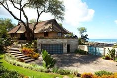 a large house sitting on top of a lush green field next to the ocean and trees