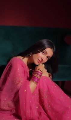 a woman in a pink sari sitting on the ground with her hands clasped to her chest