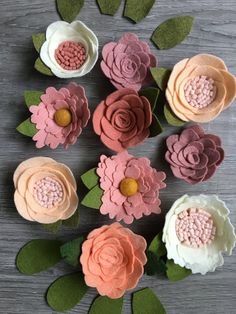 paper flowers are arranged on a table with green leaves and pink ones in the middle