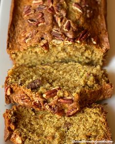 sliced loaf of banana nut bread on a white platter with pecans in the background