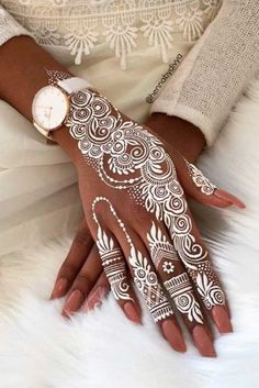 a woman's hand with henna tattoos on it and white fur around her