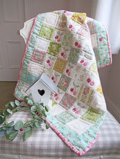 a birdhouse sitting on top of a bench next to a quilted tablecloth