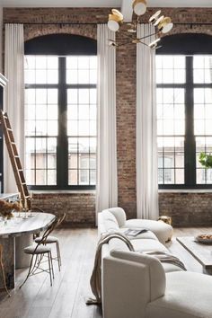 a living room filled with furniture and windows next to a dining table in front of a brick wall